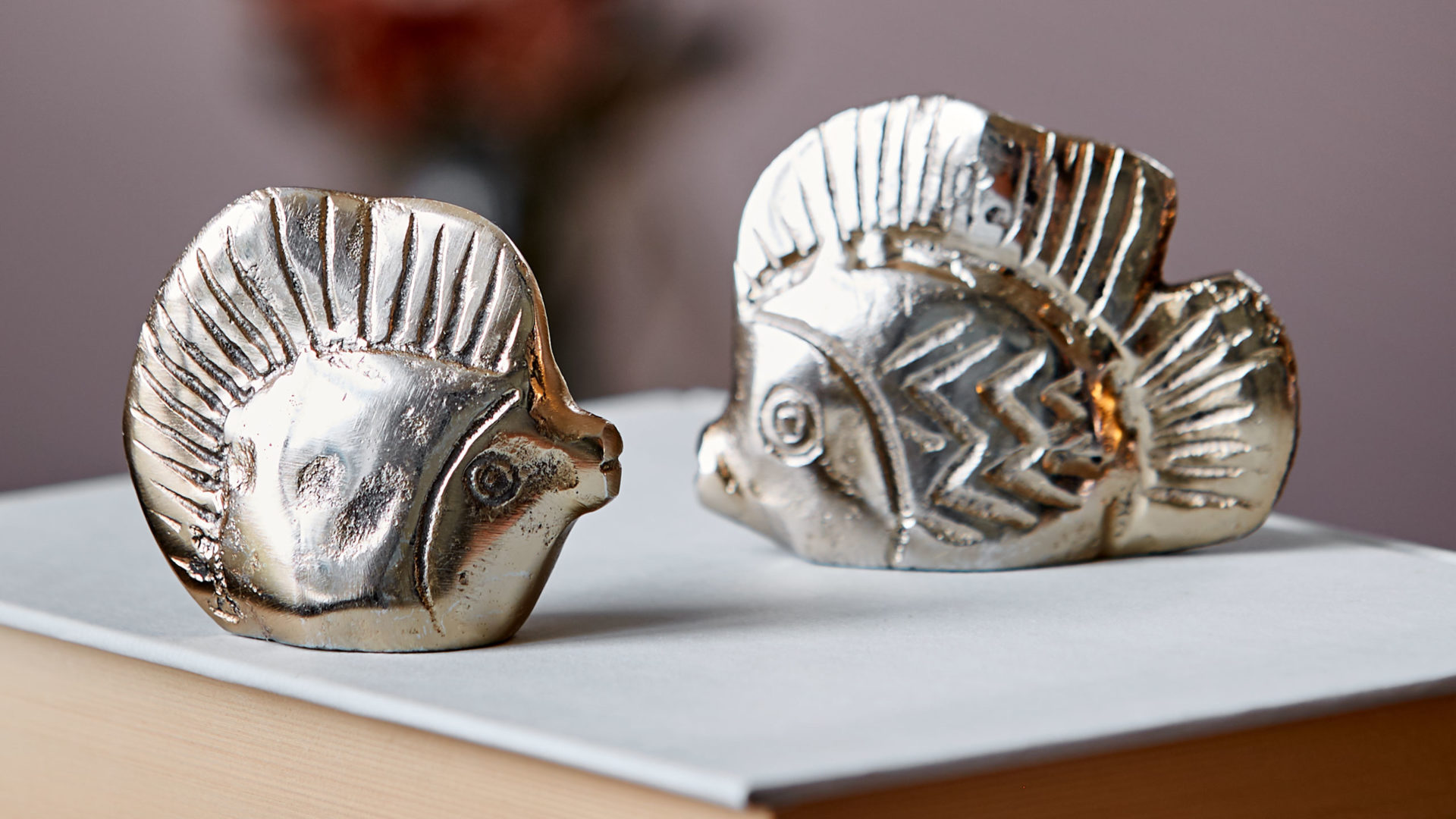 zwei sika design fisch glücksbringer figuren auf einem buch