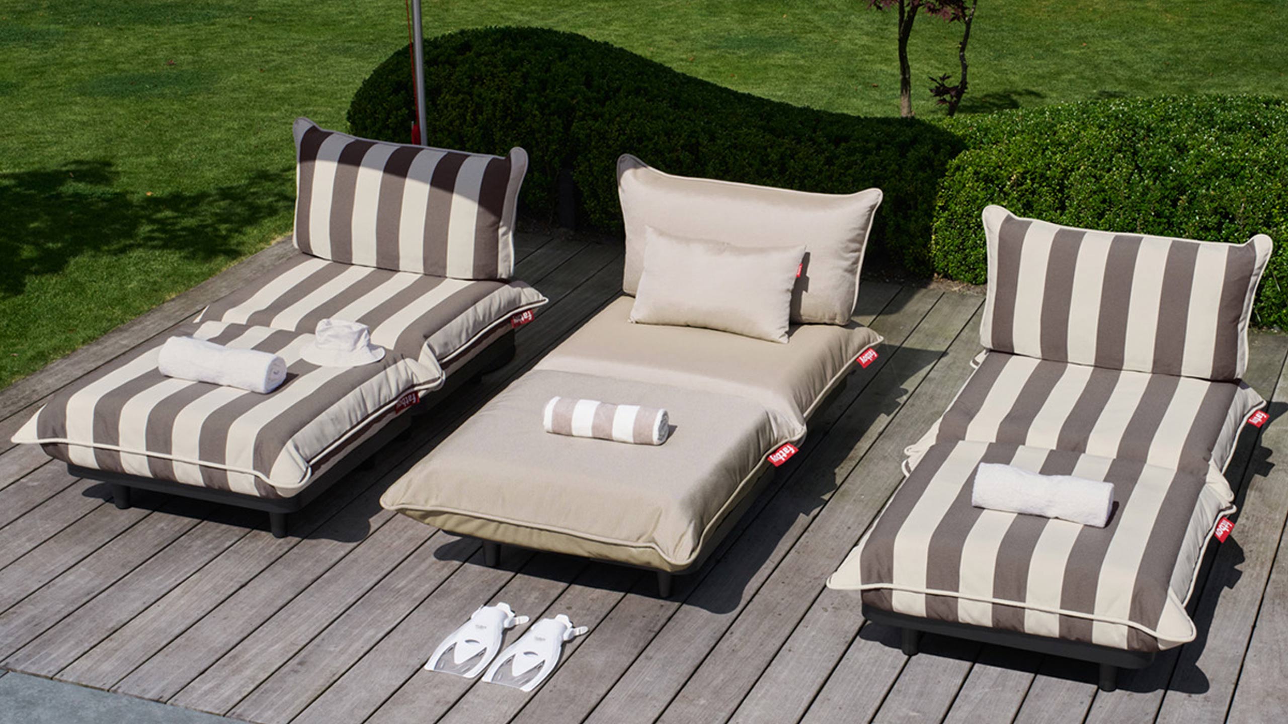 drei fatboy paletti outdoormöbel in creme und creme-braun gestreift auf einer holzterrasse unterm sonnenschirm