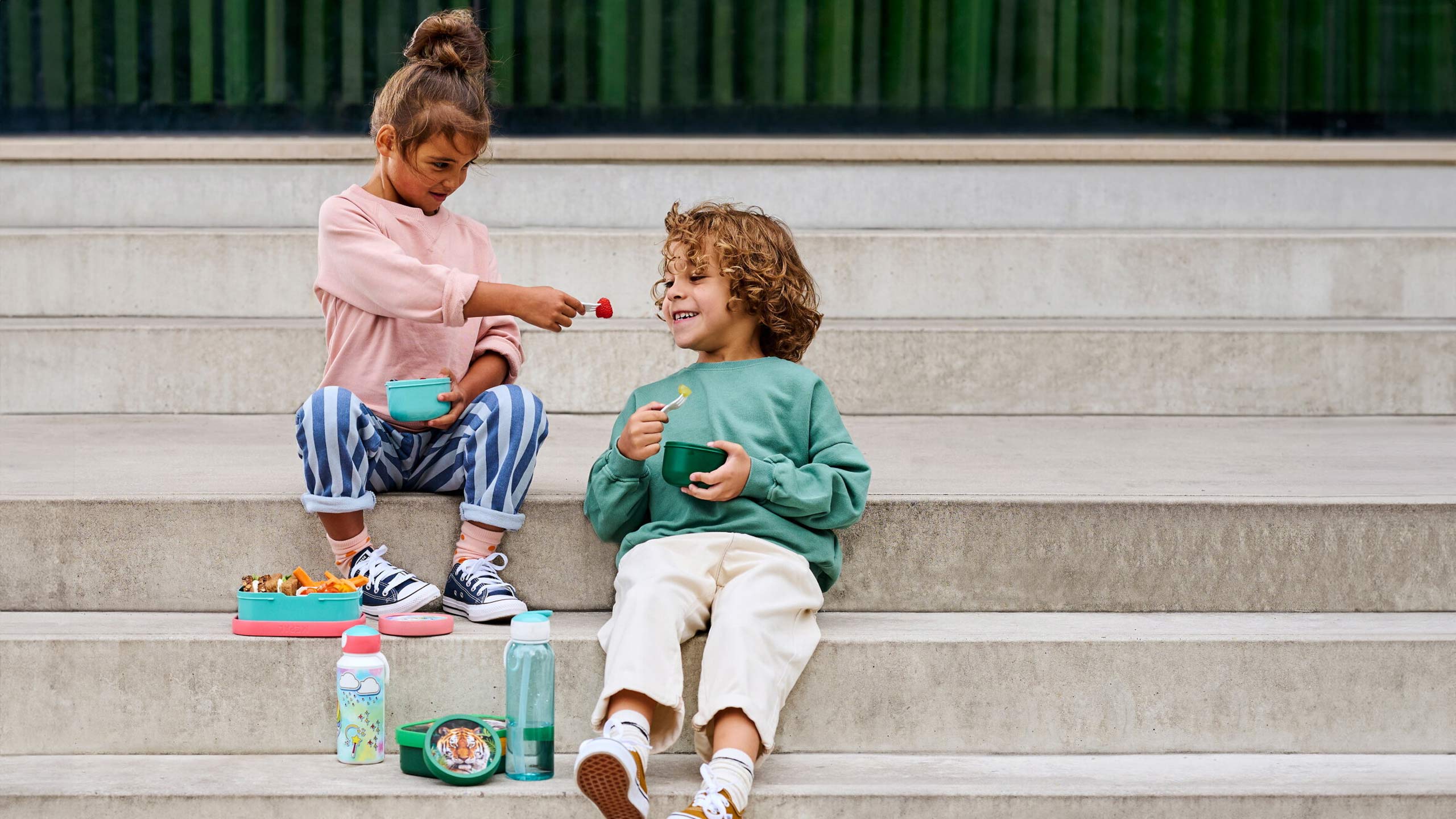 zwei kinder sitzen auf einer treppen und essen obst aus dem mepal campus pausenset mit brotdose und trinkflasche
