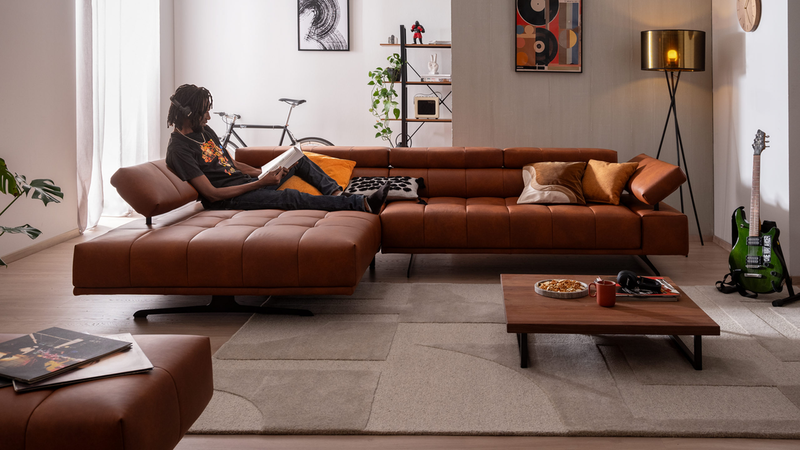 mann sitzt mit kopfhörern auf dem ada raimo sofa in braun in einem modernen wohnzimmer