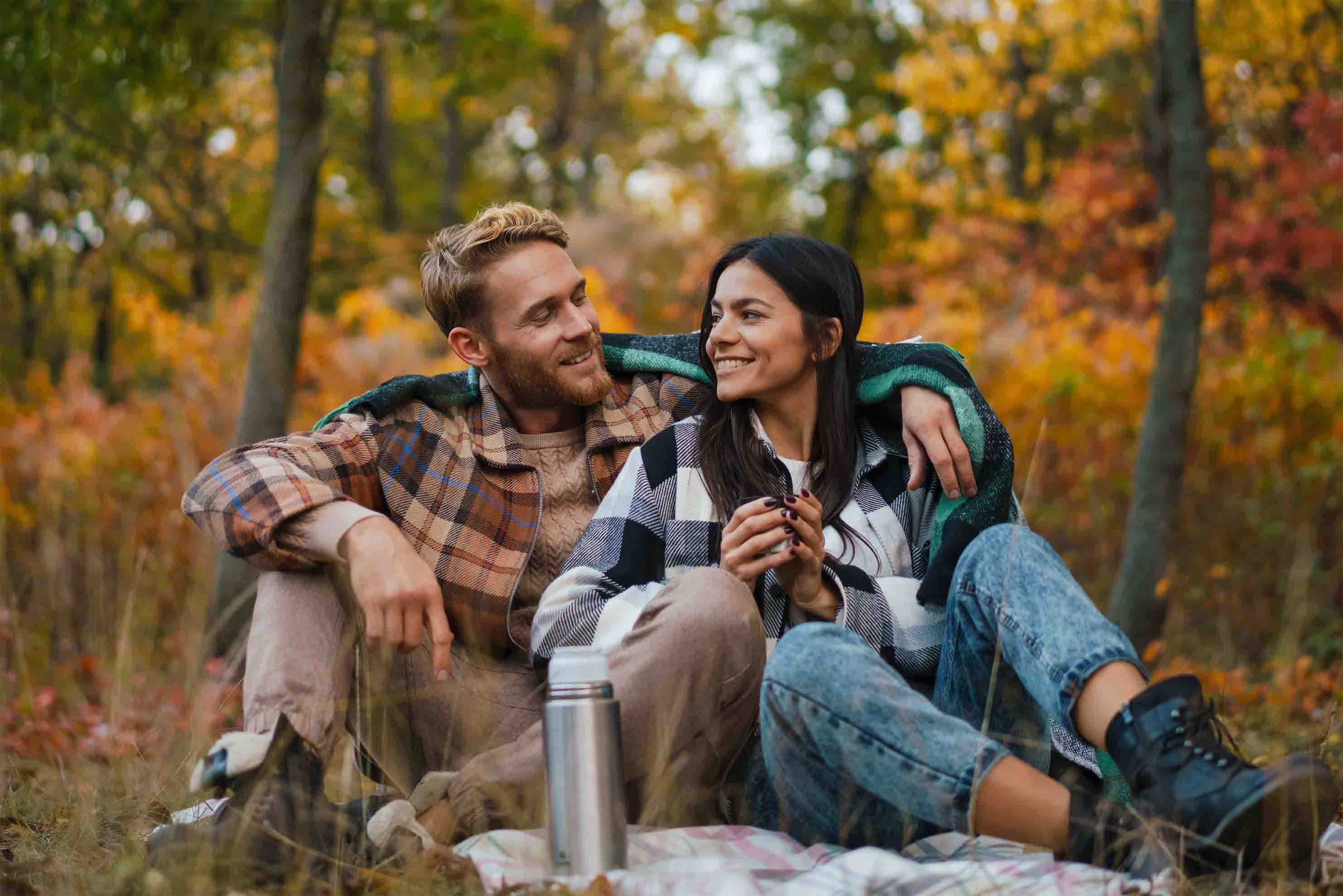 Mann und Frau an einem herbstlichen Tag schauen sich verliebt an und picknicken