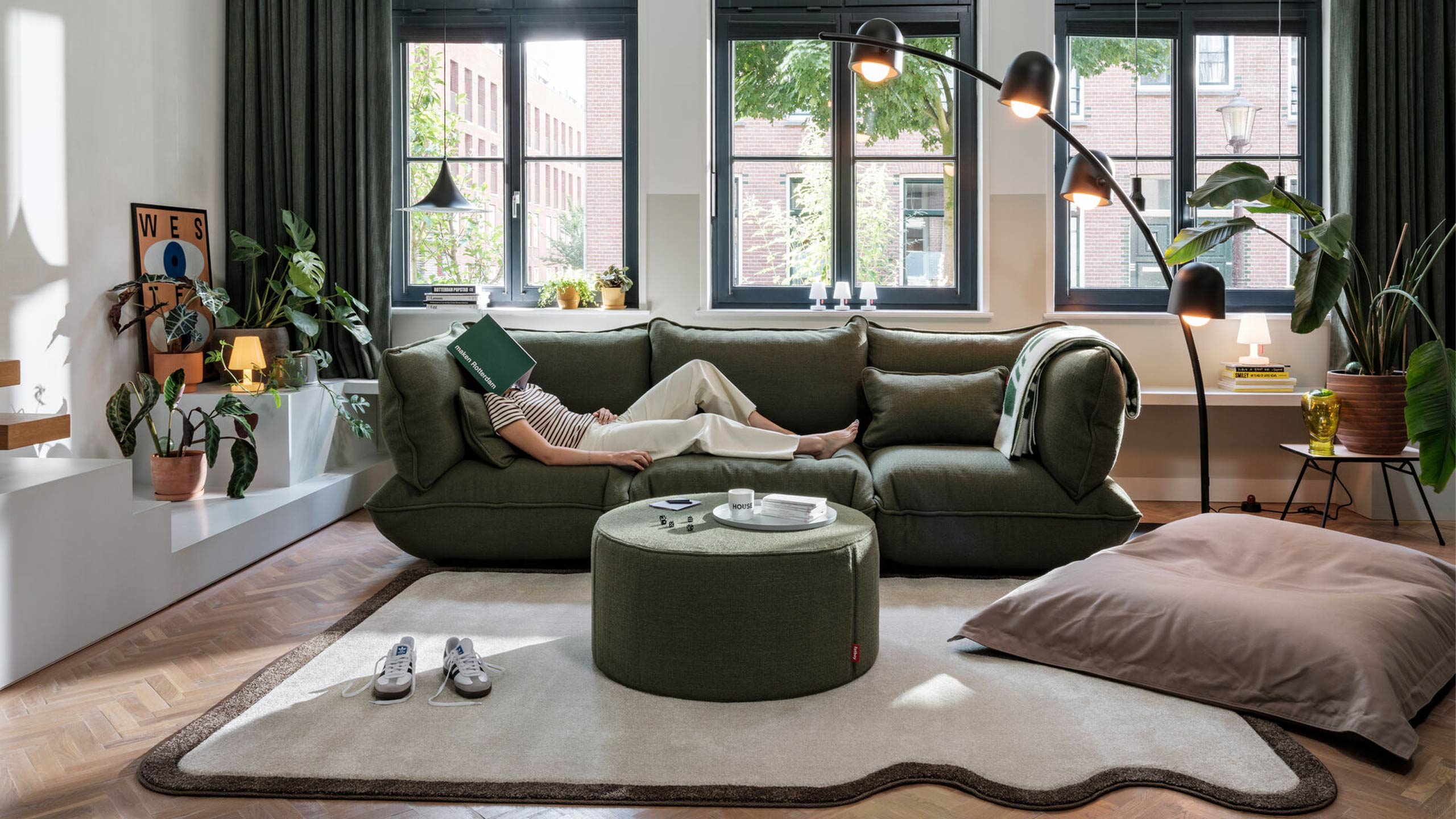 frau liegt mit buch auf dem kopf auf einem fatboy bouclesofa in grün in einem grünen wohnzimmer