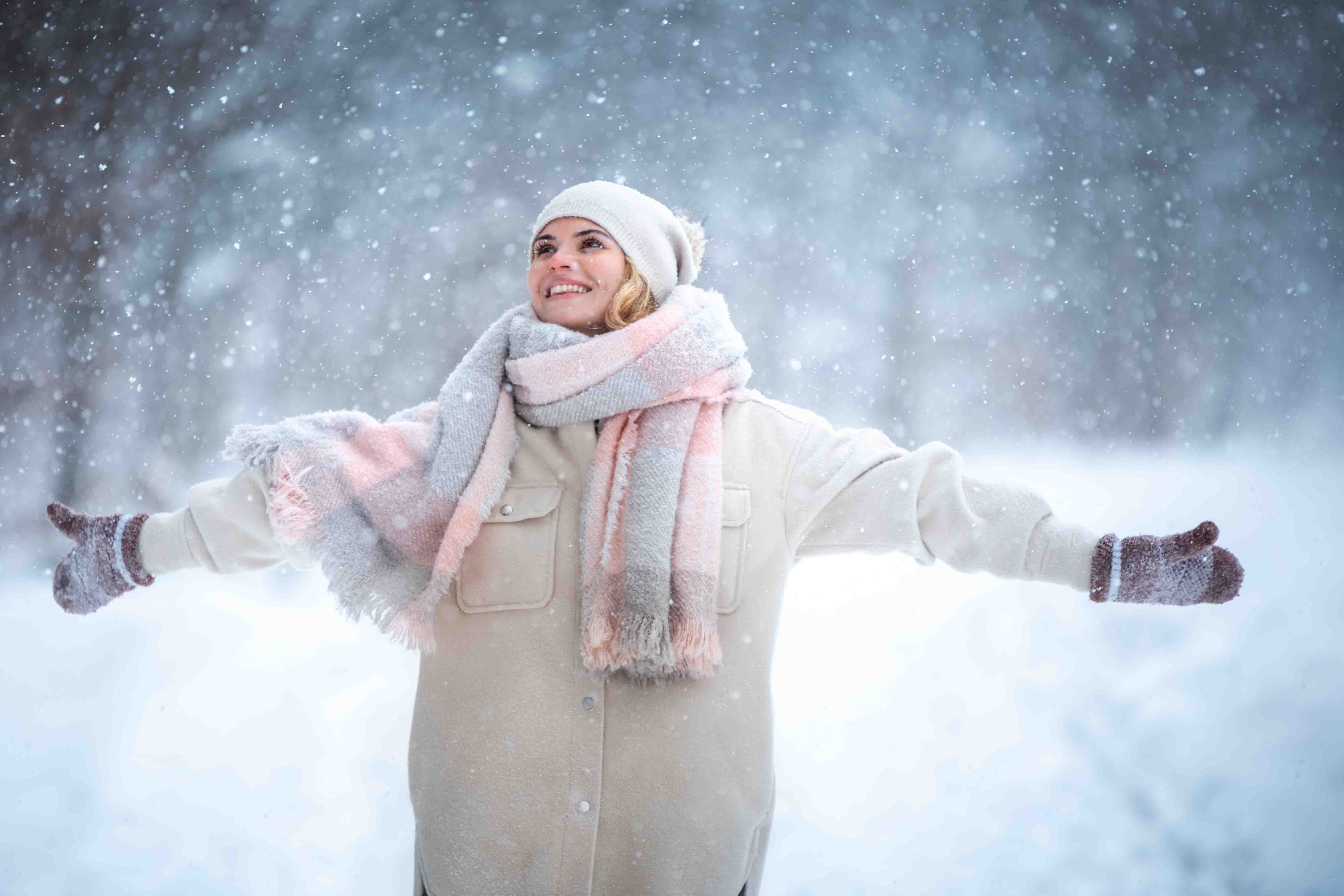 Fröhliche Frau in Winterkleidung steht armeausbreitend im verschneitem Wald