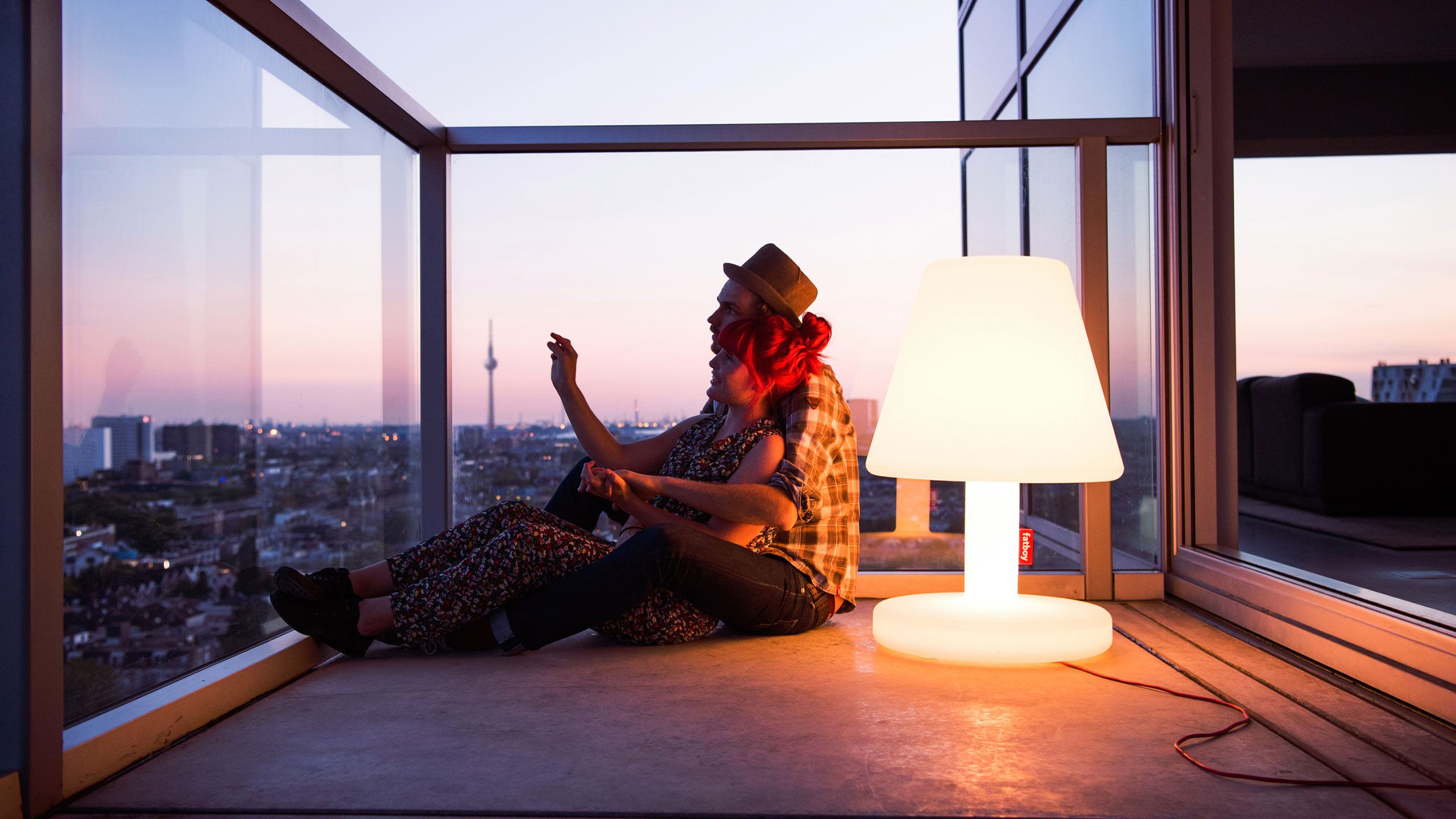 paar sitzt umschlungen auf einem balkon mit blick auf berlin neben einer fatboy edison lampe