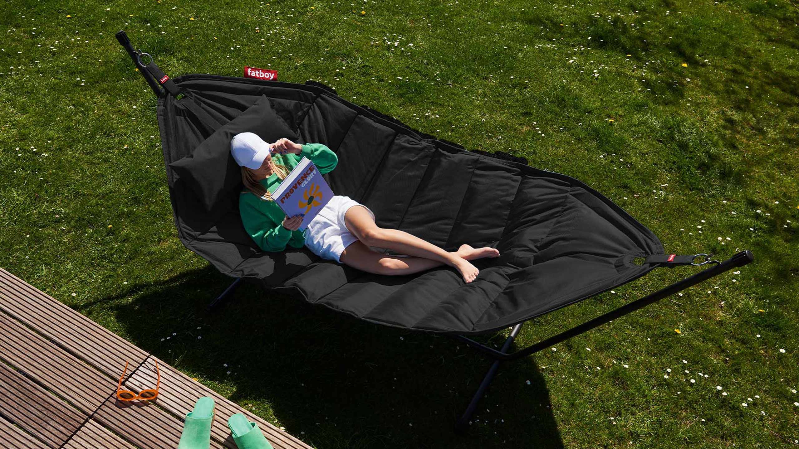 frau liest die rückseite von einem buch und liegt auf einer schwarzen fatboy headdemock hängematte auf einer wiese