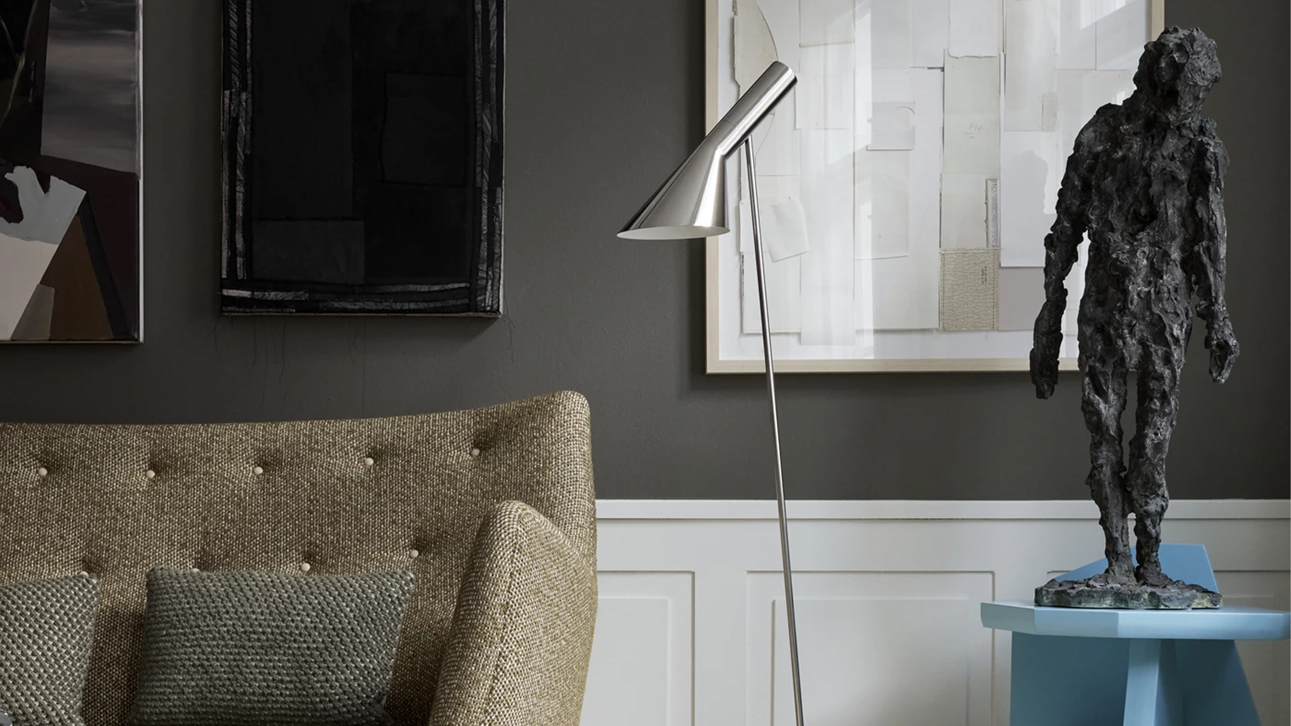 louis poulsen aj stehleuchte aus edelstahl neben einem sofa und einer schwarzen skulptur