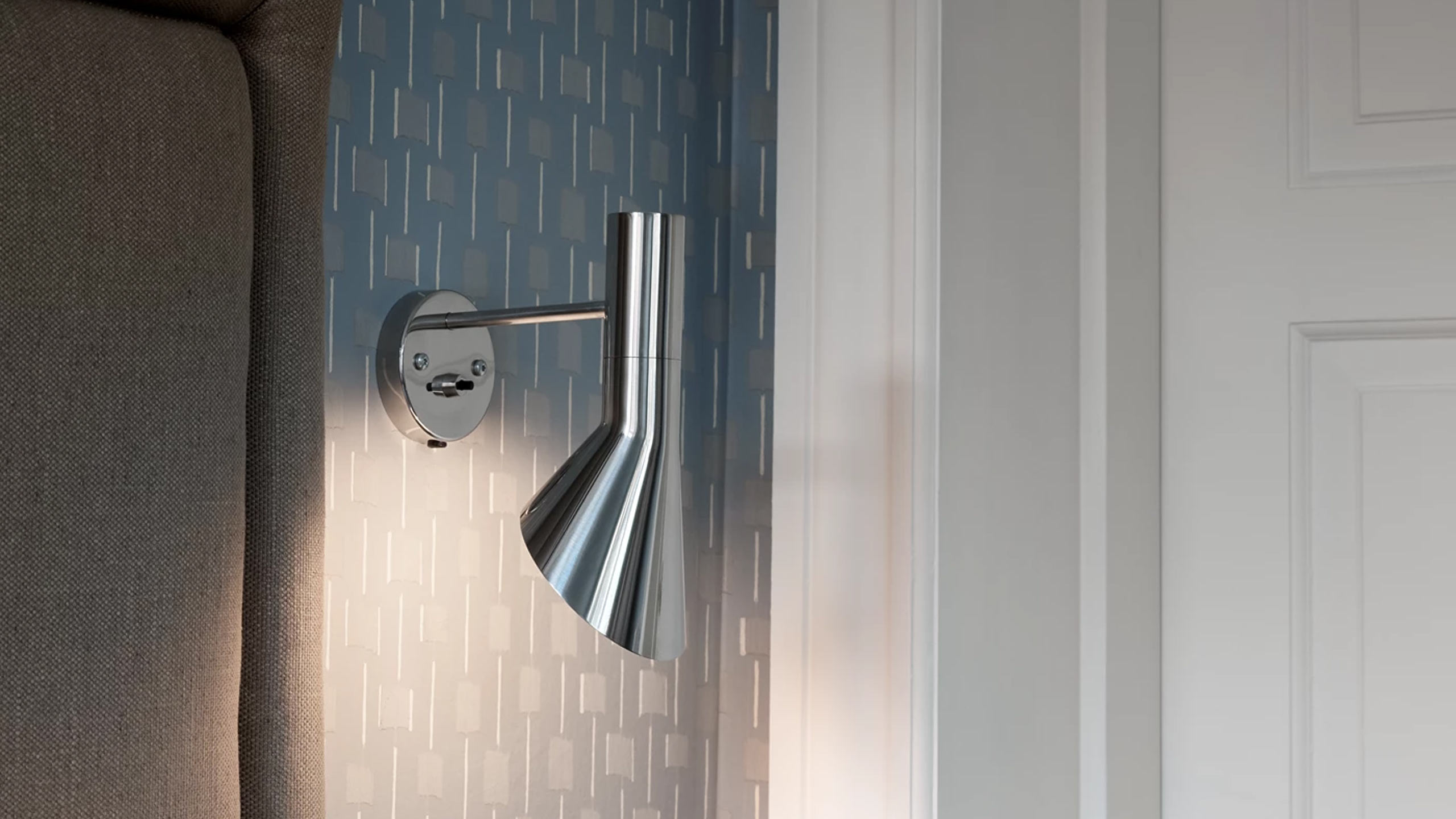 louis poulsen aj wandleuchte aus edelstahl an einer grauen wand im schlafzimmer