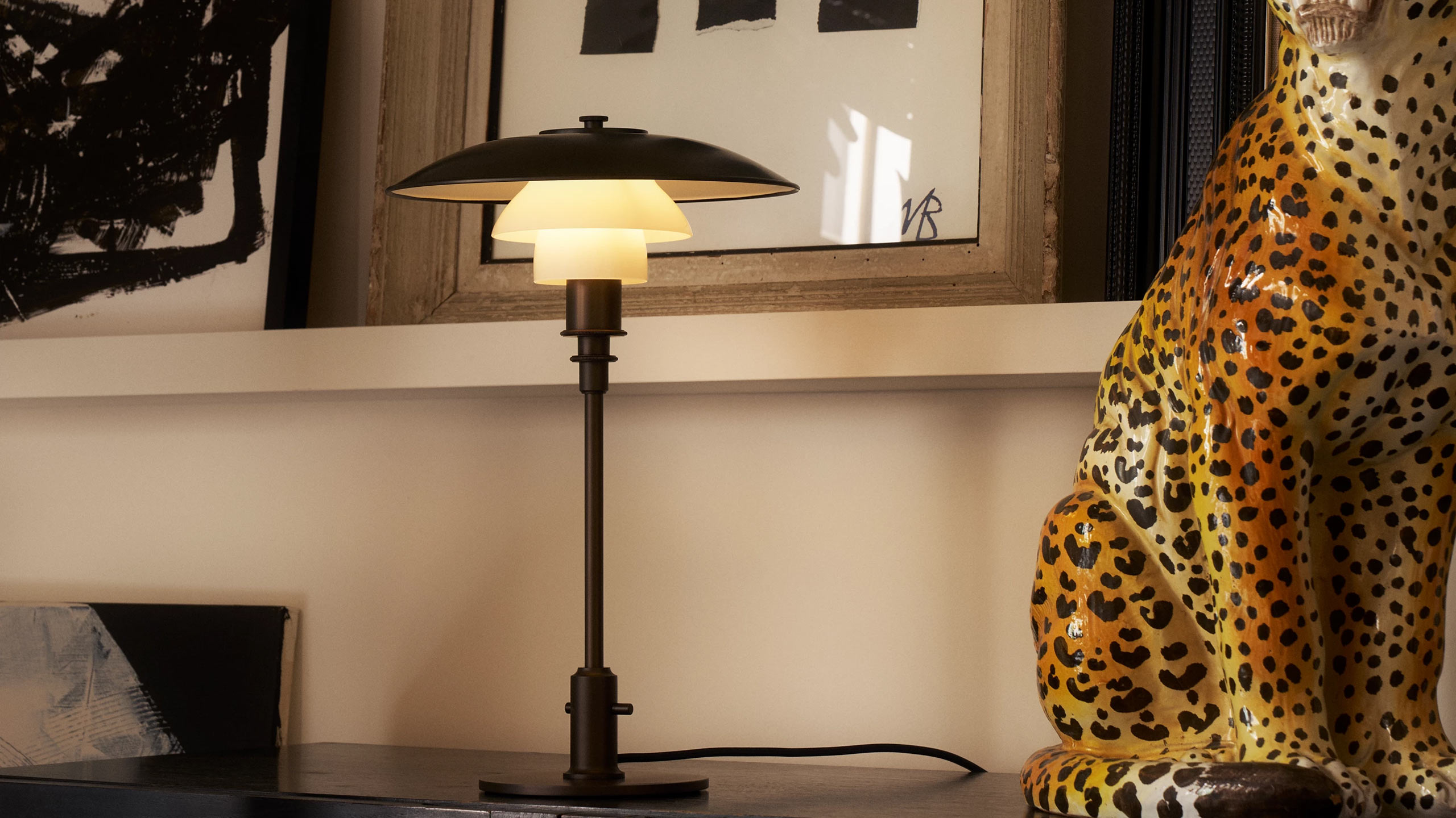 louis poulsen ph 3/2 tischleuchte aus messing neben einer großen leoparden figur auf einem sideboard