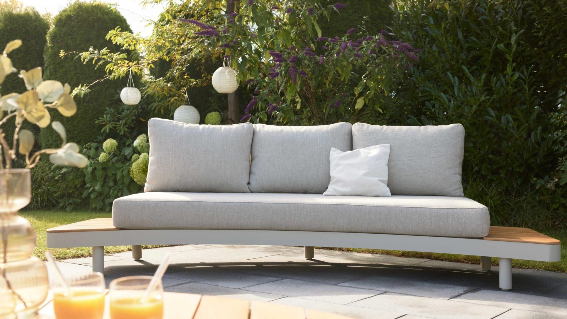 interliving 7015 teak loungesofa in hellgrau auf einer terrasse vor grün